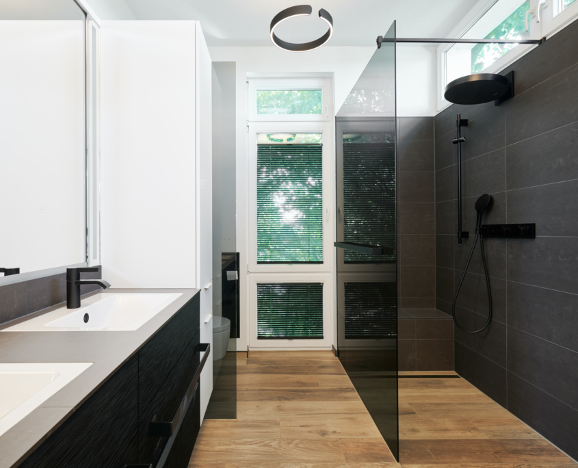 Modernisiertes Badezimmer in einem Haus im Sauerland mit bodengleicher Dusche, schwarzen Armaturen von Gessi und großformatigen Fliesen in Natursteinoptik.